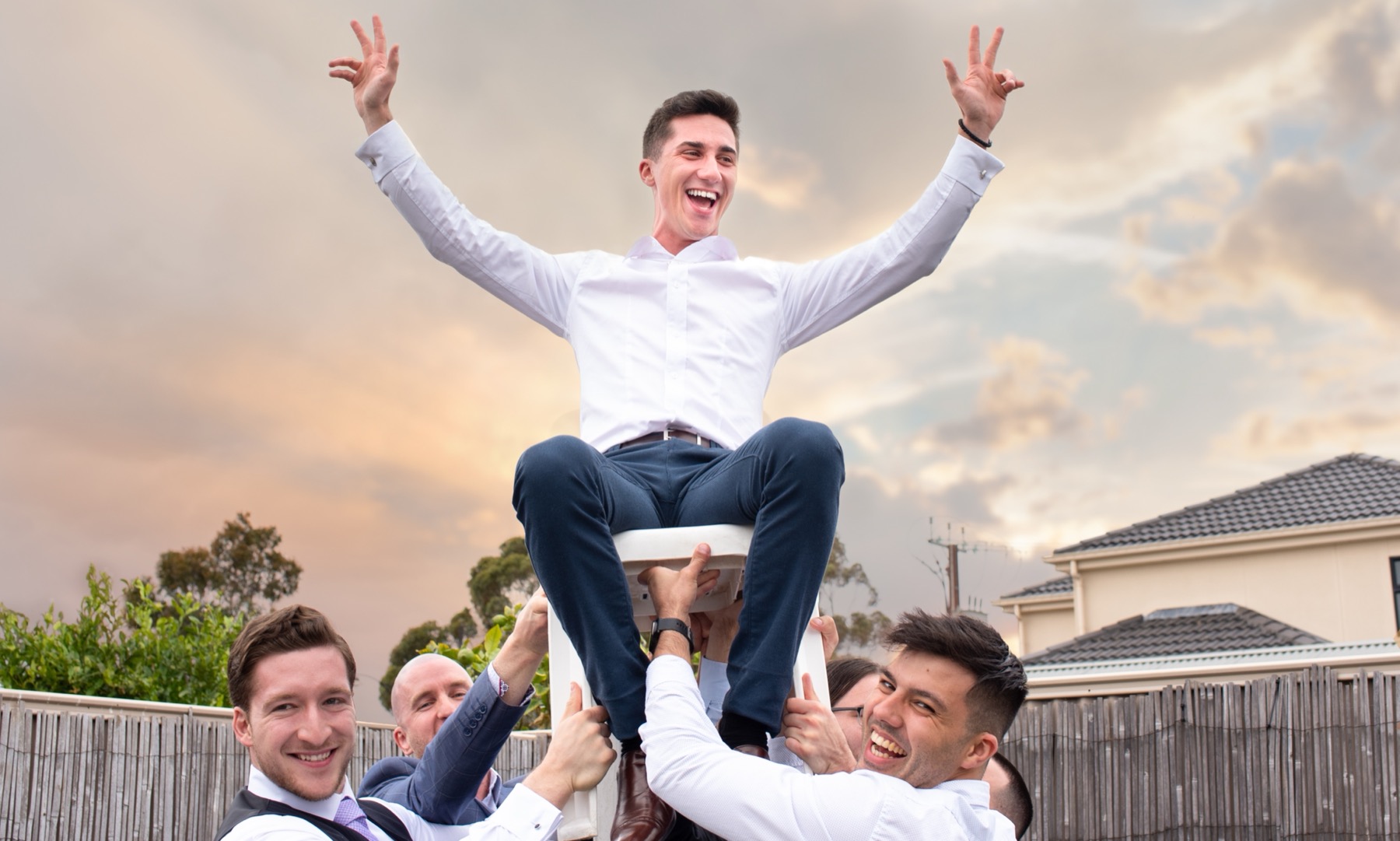 Miljan hoisted up on a chair by friends at sunset